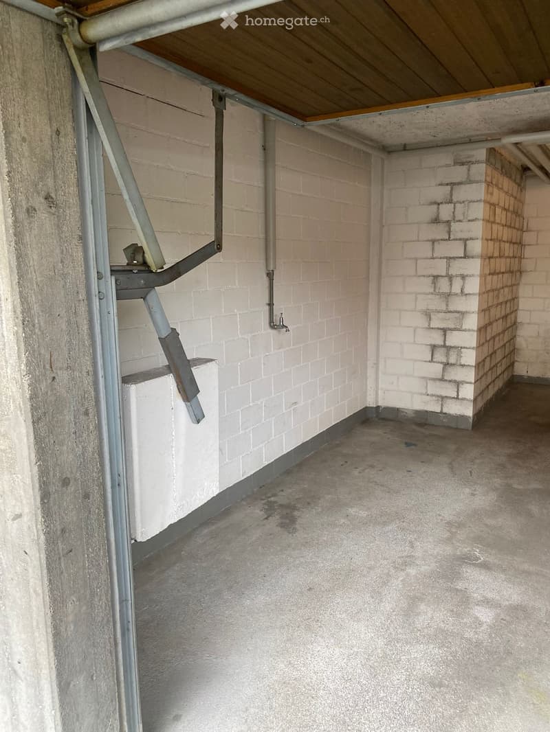 Empty room with white brick walls, concrete floor, metal staircase, and exposed pipes.
