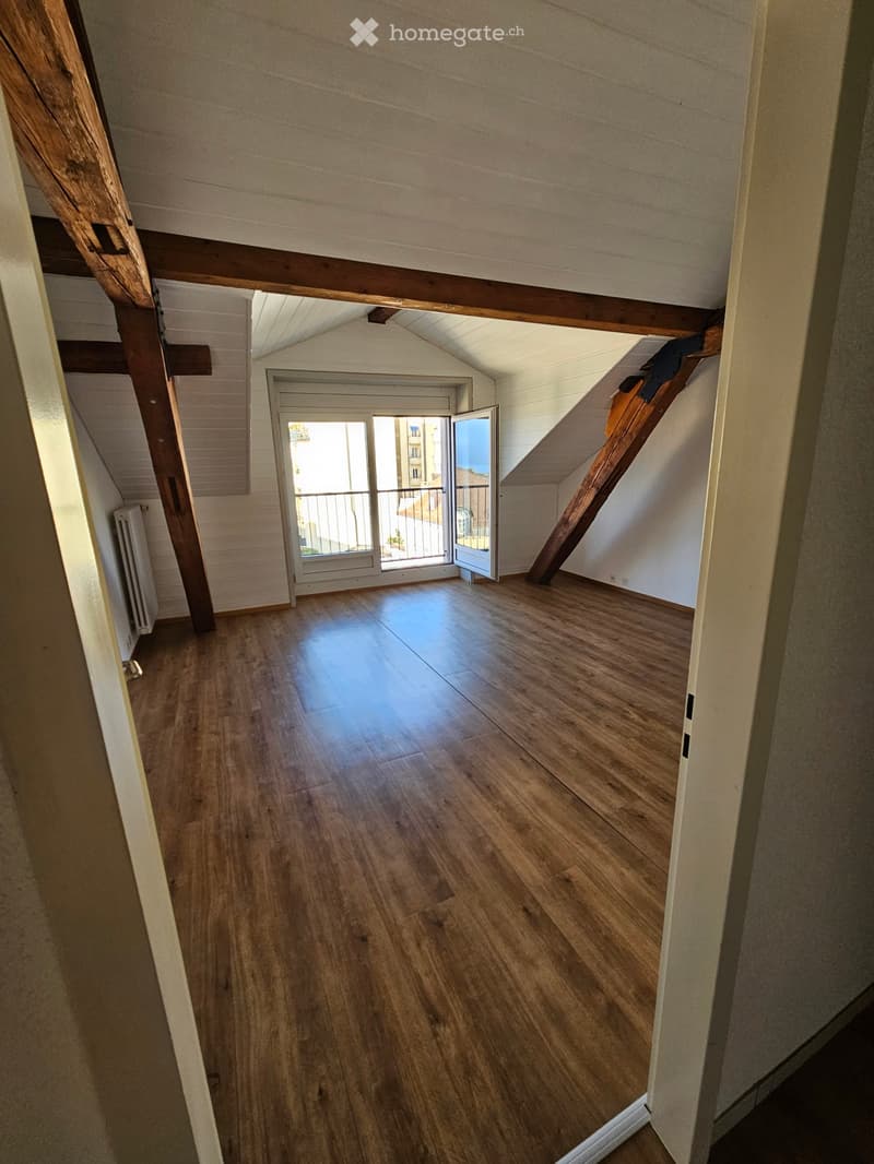 Empty attic space with wooden flooring, exposed wooden beams, and a door leading to a balcony.