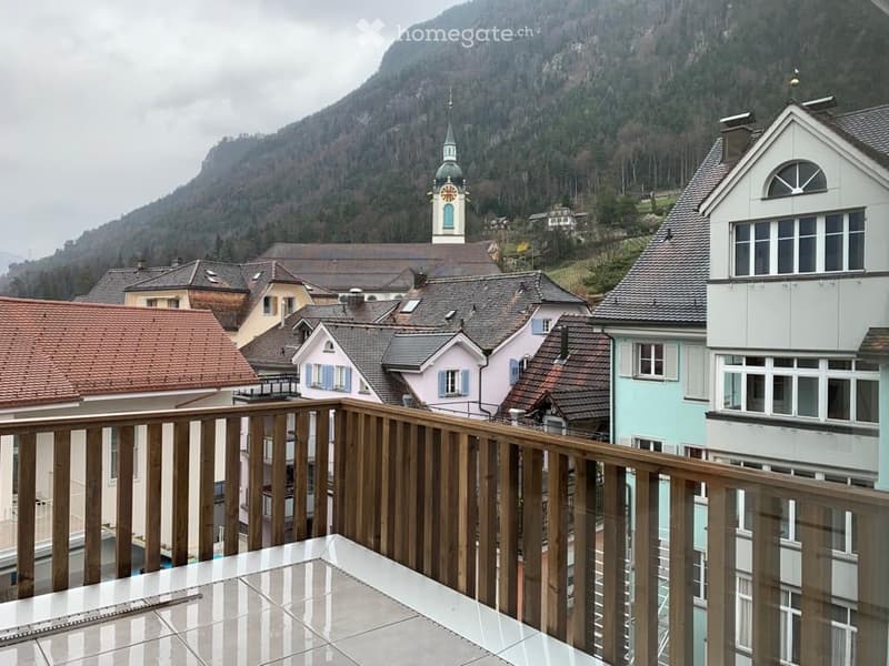 Balcony overlooking a picturesque town with colorful houses, a church tower, and a mountain backdrop.