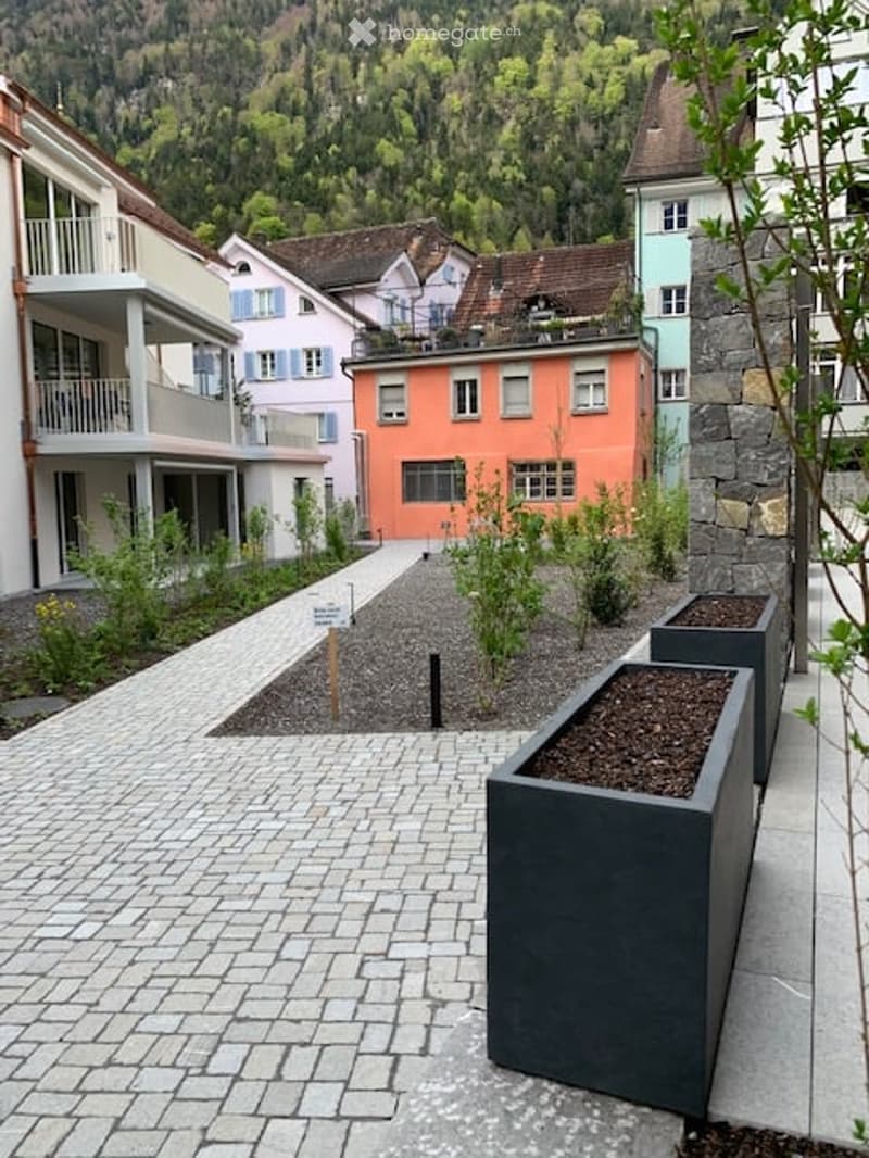 A paved outdoor area with modern planters, surrounded by residential buildings and greenery.
