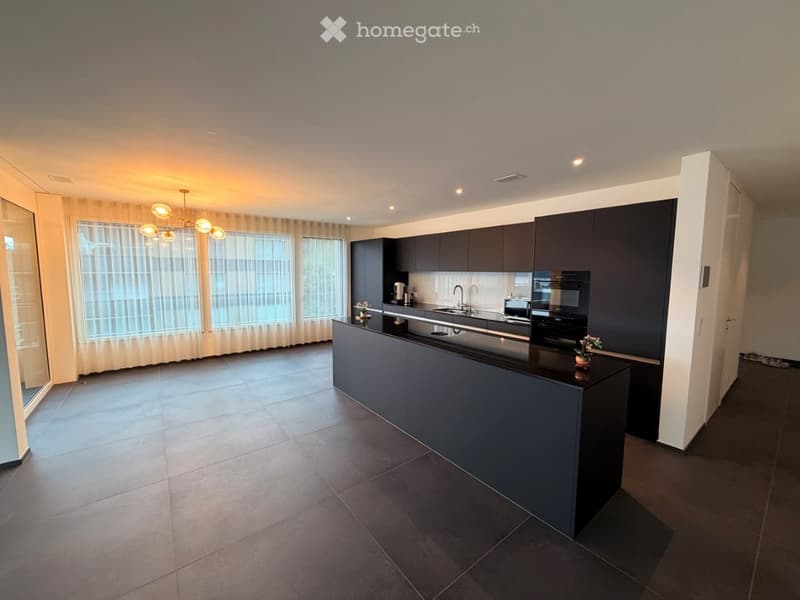 Modern kitchen with dark cabinetry, a central island, stainless steel sink, and a chandelier with multiple lights.