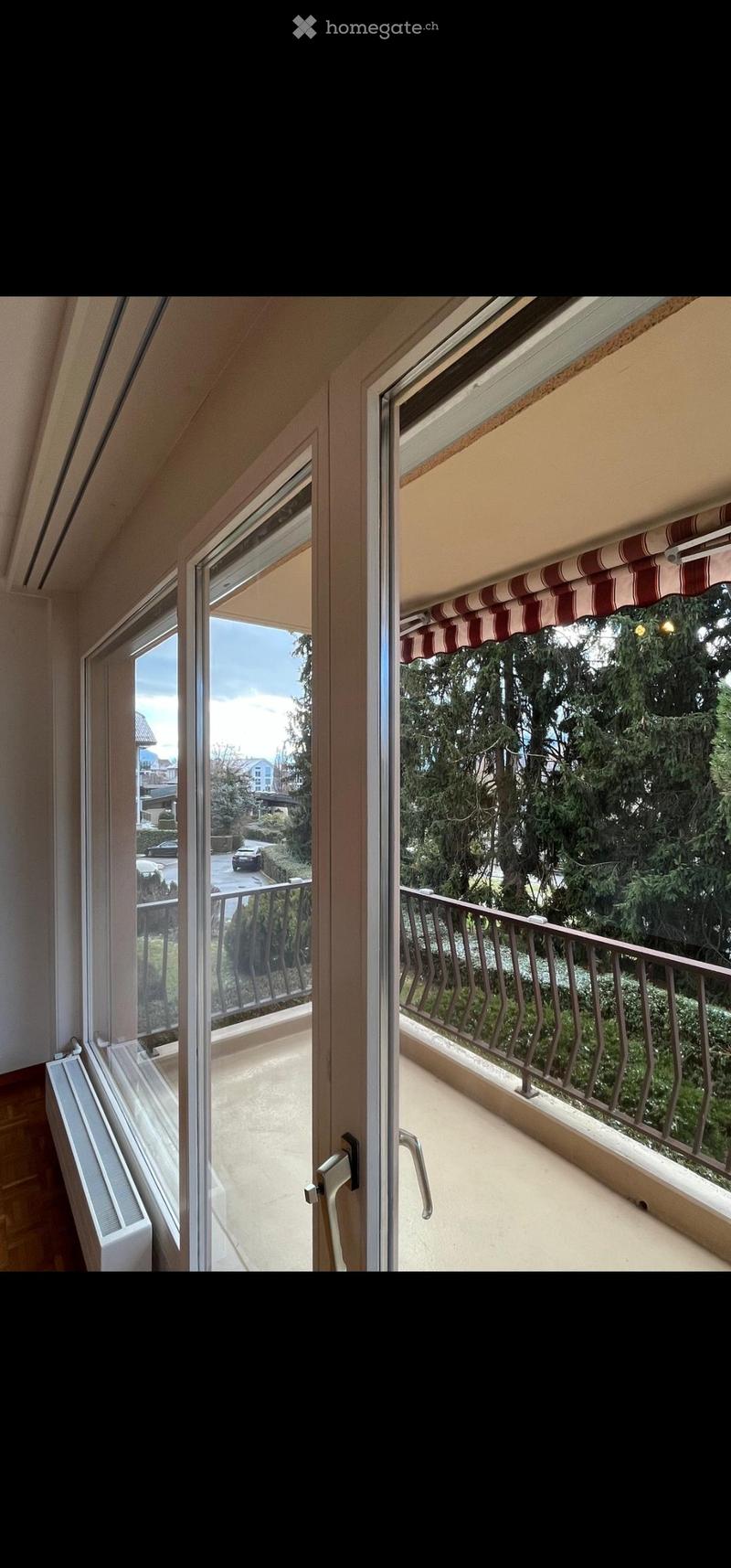 Balcony with metal railing, striped awning, and view of greenery and street.