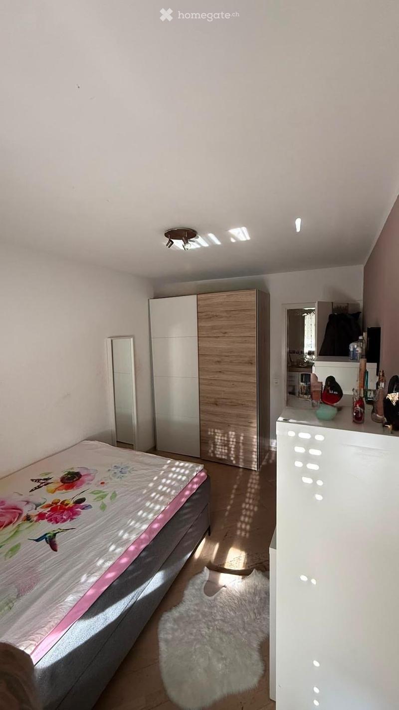 A modern bedroom with a double bed, a large wardrobe, a mirror, a furry rug, and a dresser with various items on top.