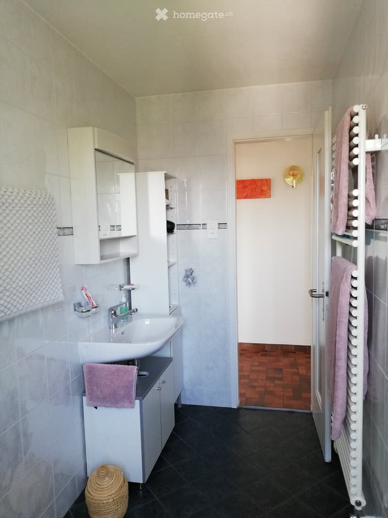 Modern bathroom with white tiles, dark floor, sink, mirror, towel rack, and wicker basket.