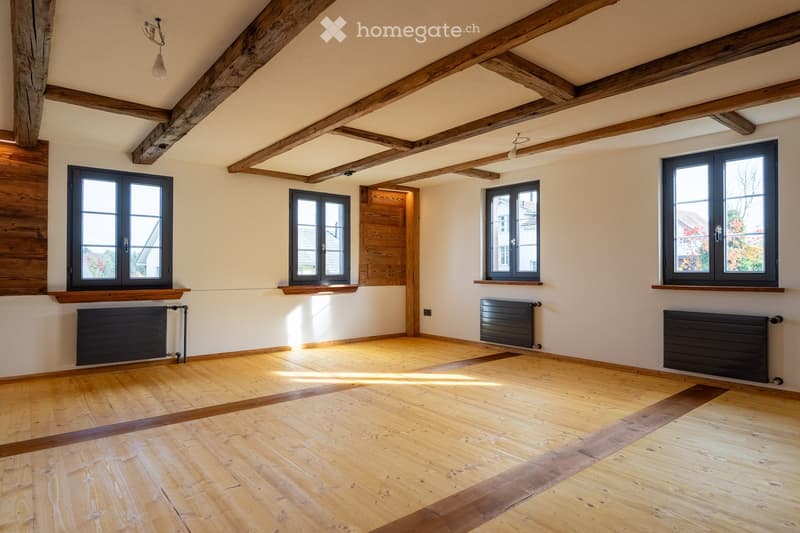 Empty room, wooden floors, white walls, wooden beams on ceiling, radiators, windows with white frames