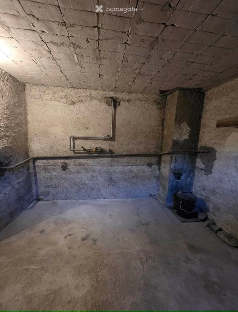 Empty basement or utility space with concrete walls and floor, exposed pipes, and a small black container in the corner.