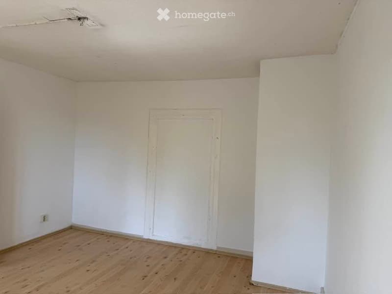Empty room with wooden flooring, white walls, and a single door.
