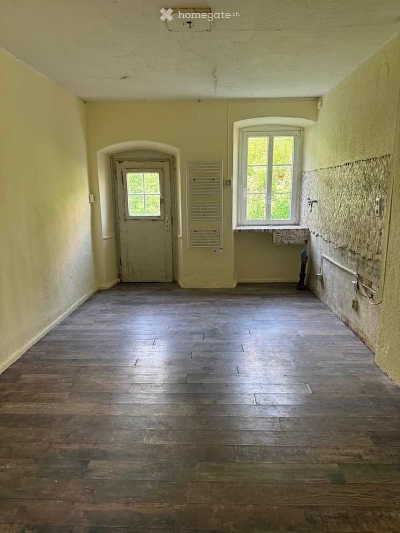 Empty hallway with wooden flooring, arched doorways, and windows allowing natural light.