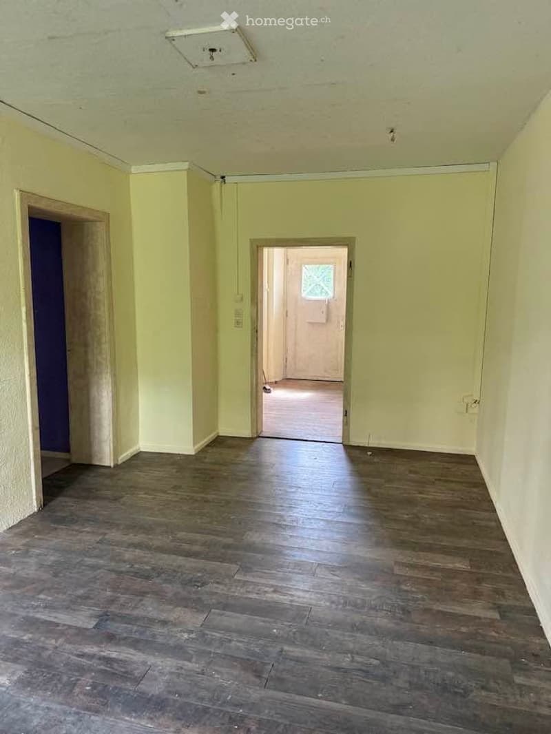 Empty hallway with wooden flooring, cream-colored walls, and two open doorways leading to other rooms.