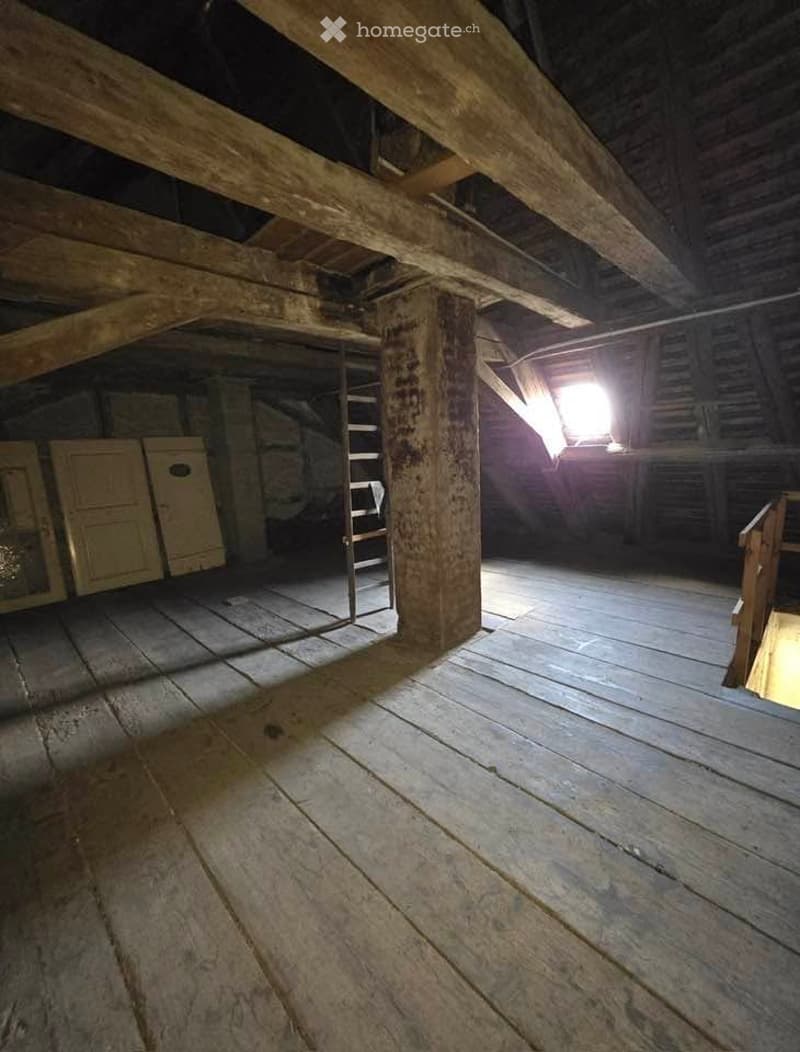 Empty attic space with wooden beams, exposed wooden floor, and minimal built-in storage. No furniture or equipment present.