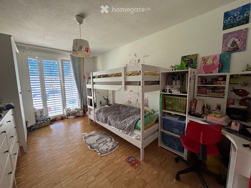 Cozy children's bedroom with a bunk bed, desk, shelves, and colorful decorations.
