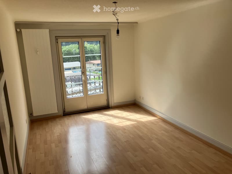 Empty room with wooden flooring, white walls, and a sliding glass door leading to a balcony.