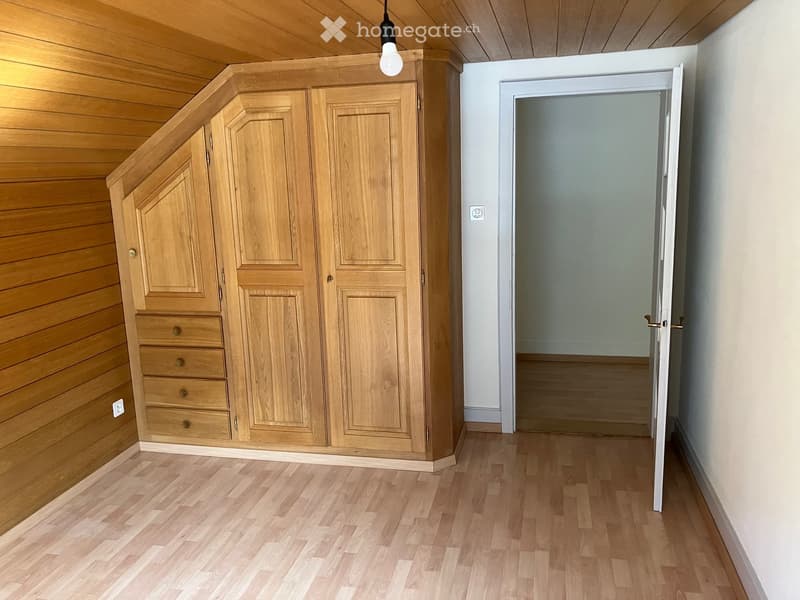 Empty hallway with wooden flooring, white walls, and a large built-in wooden wardrobe with multiple doors and drawers on the left side.