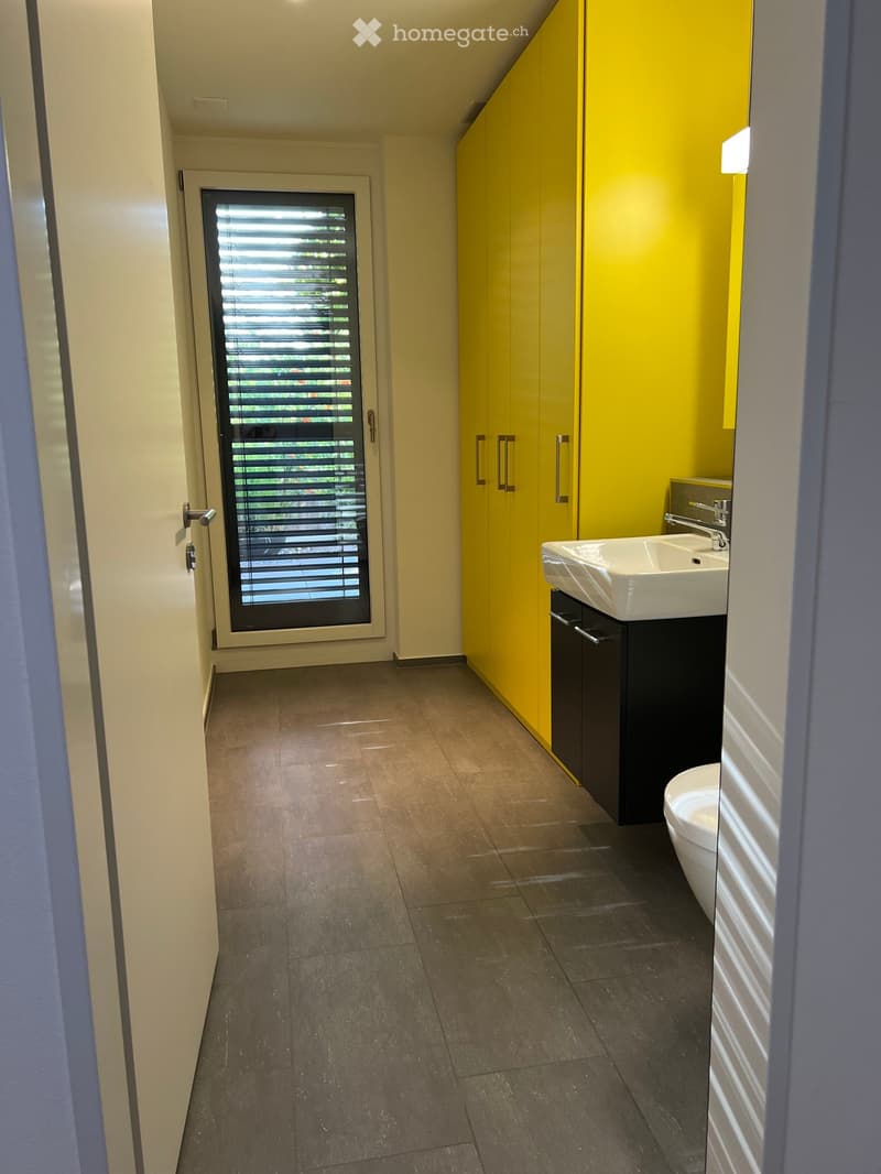 Modern bathroom with yellow cabinets, white sink, and toilet. Features a window with blinds and tiled flooring.