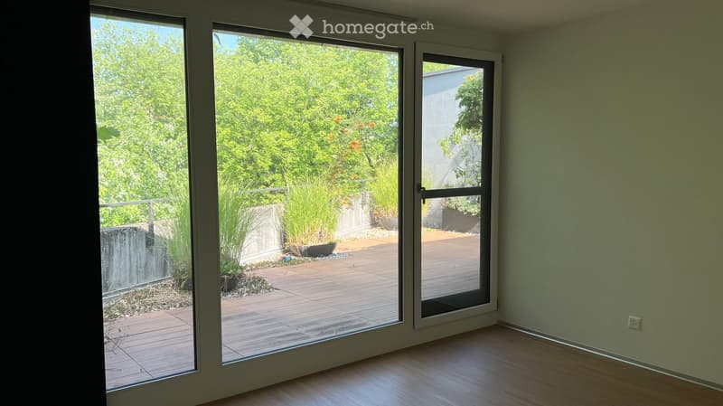 Empty room with wooden flooring and large glass sliding doors leading to a wooden deck and garden area.