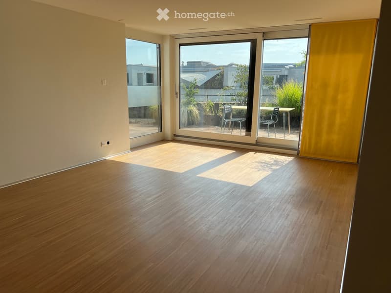 Empty room with wooden flooring and large sliding glass doors leading to a balcony area with outdoor furniture.