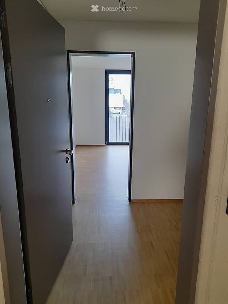 Empty hallway with wooden flooring, leading to a balcony area with a metal railing.