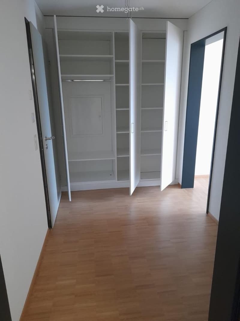 Empty room with wooden flooring, white walls, and an open closet with empty shelves and hanging space.
