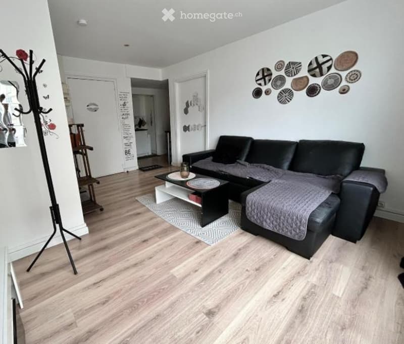 Modern living room with light wooden flooring, black sectional sofa, coffee table, decorative rug, and wall art featuring circular designs.