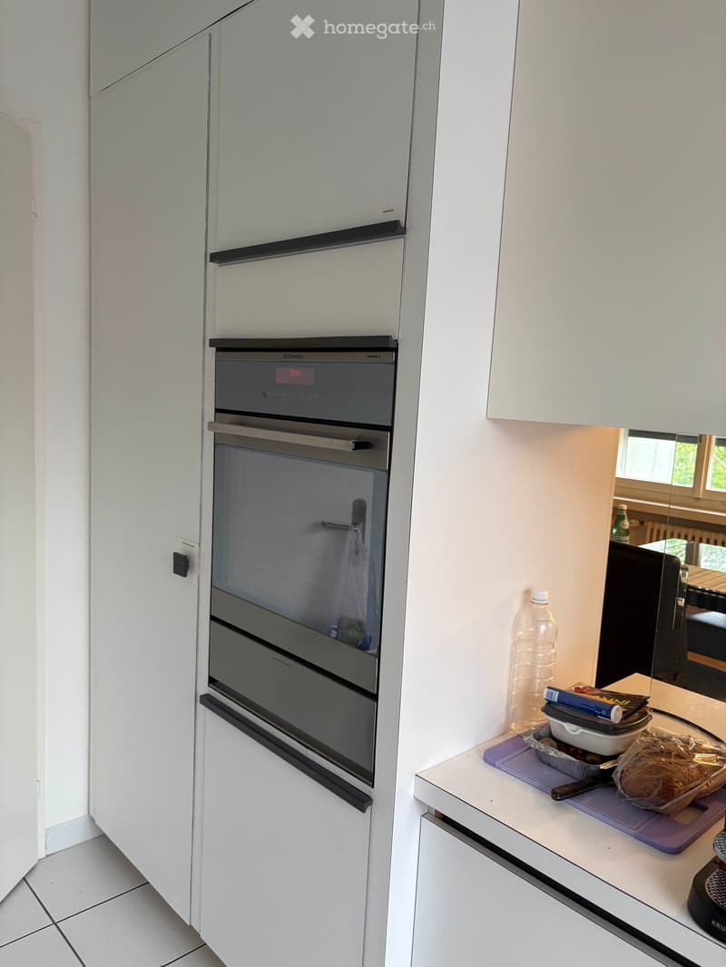 Modern kitchen with white cabinets, stainless steel oven, countertop with cutting board, bread, bowl, and knife.