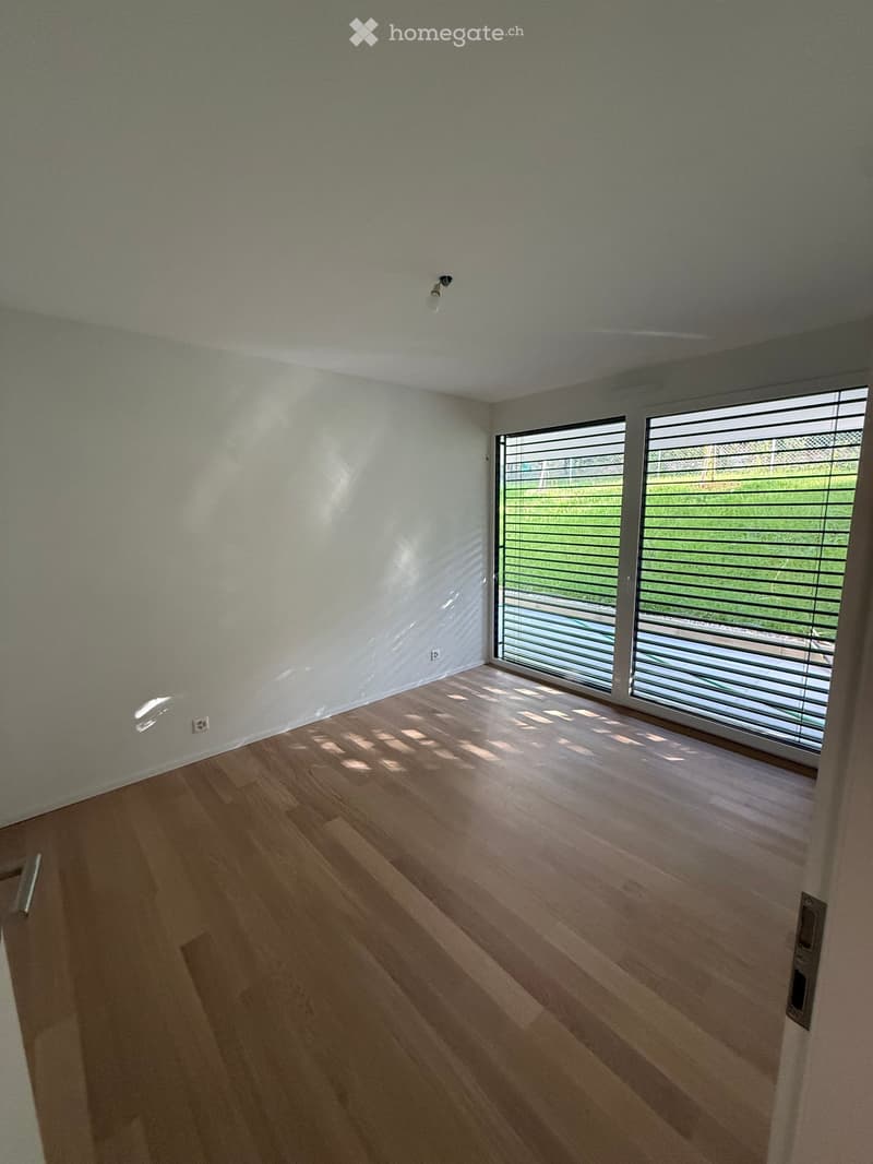 Empty room with light-colored walls, wooden flooring, and large sliding glass doors leading to an outdoor area.