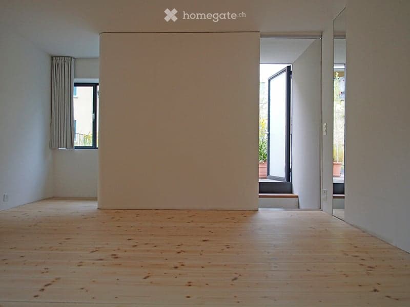 Empty room with wooden flooring, white walls, and large windows with curtains. No furniture or equipment present.