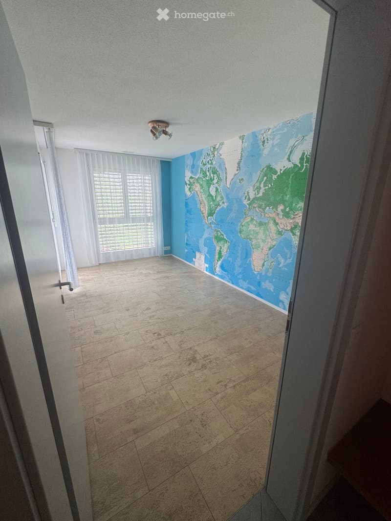 Empty room with tiled floor, white walls, large world map mural, and white curtains covering windows.
