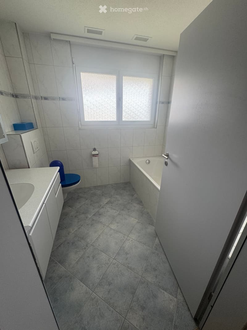 Modern bathroom with grey tiled floor, white walls, bathtub, toilet, sink, and cabinet.