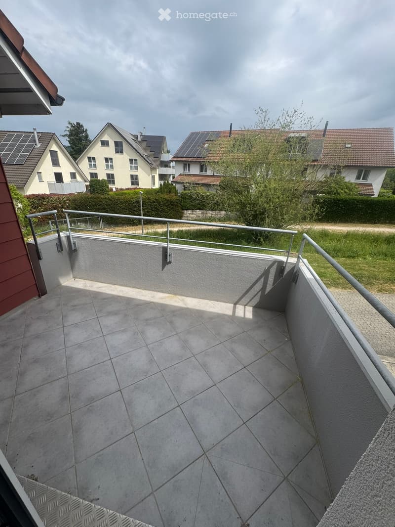 Balcony with tiled floor, metal railing, and view of neighboring houses and greenery.