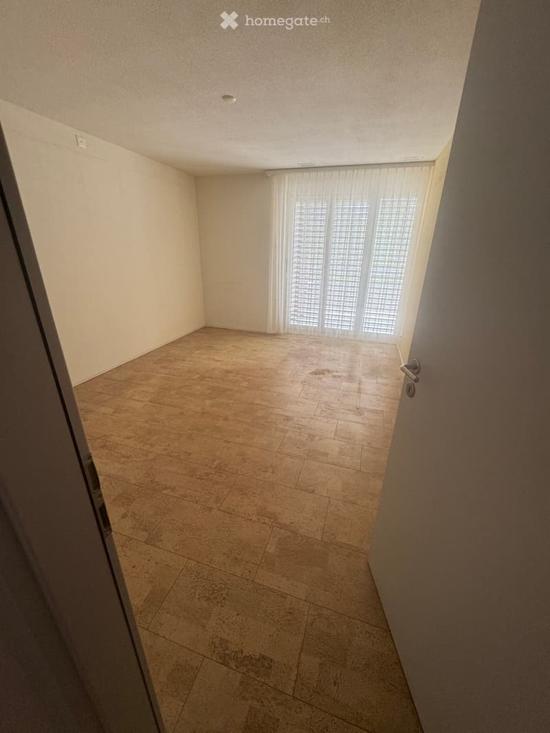Empty room with beige tiled floor, white walls, and large window with blinds. No furniture or equipment present.