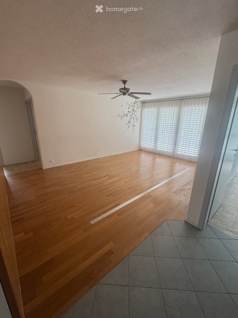 Empty room with wooden flooring, large windows with blinds, and a ceiling fan. No furniture or equipment present.