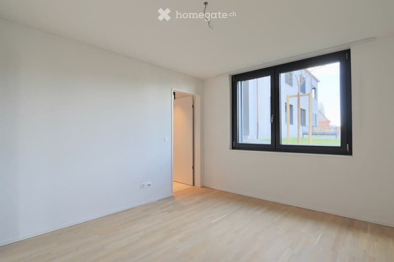 Empty room with light-colored wooden flooring, white walls, and a large window with black frame. There is a doorway leading to another room.