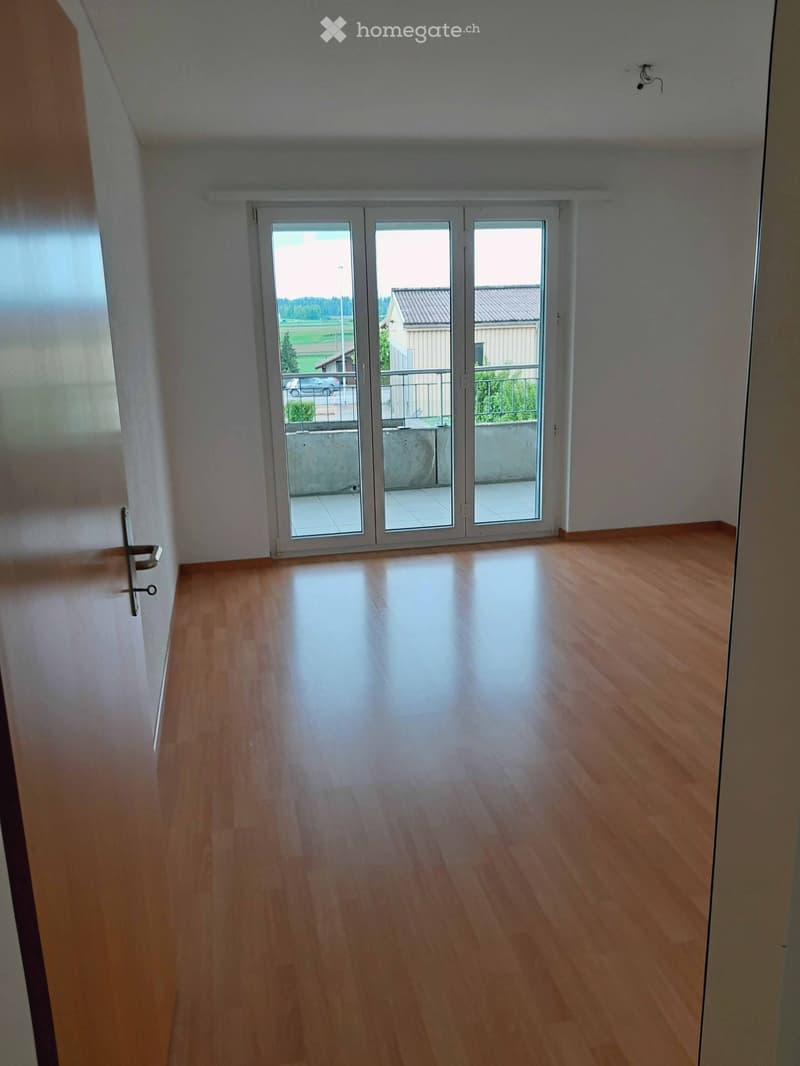 Empty room with wooden flooring, white walls, and large sliding glass doors leading to a balcony.