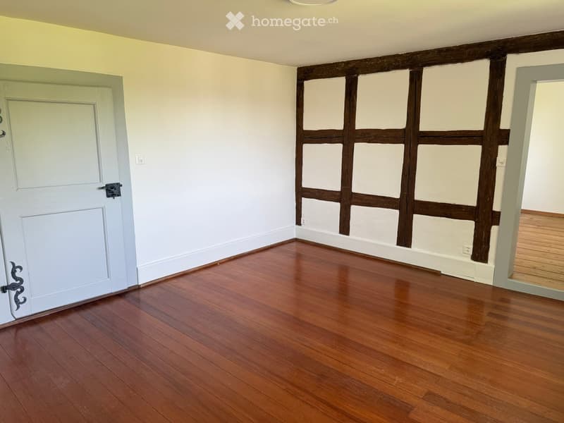 Unfurnished Room. Empty room with wooden flooring, white walls, and a door. Exposed wooden beams on one wall.