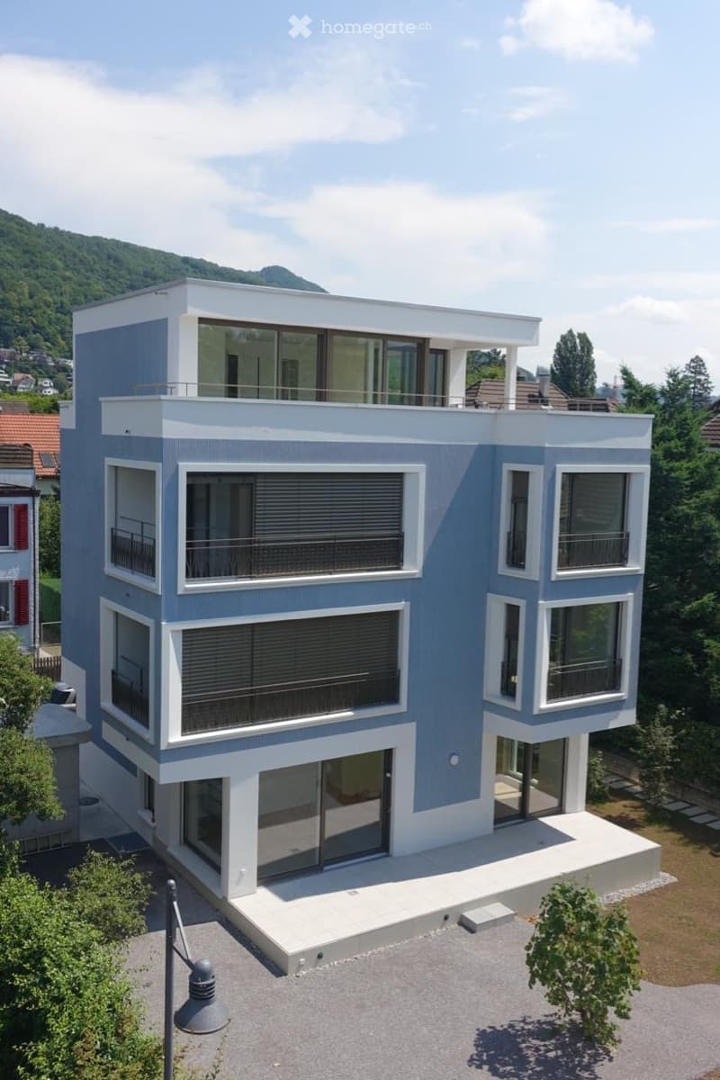 Modern two-story house with blue and white exterior, large windows, balconies, and a scenic mountain view in the background.
