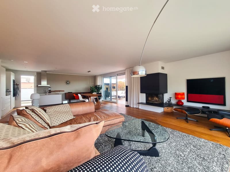 Modern living room with a large sectional sofa, glass coffee table, fireplace, flat-screen TV, and dining area visible through an open-concept layout.
