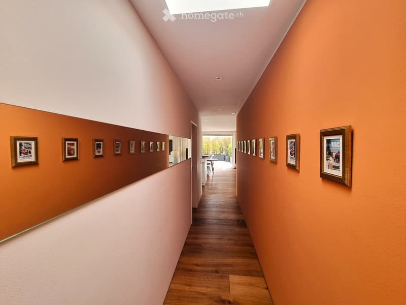 A modern hallway with wooden flooring, colorful walls, and framed artwork displayed on both sides.