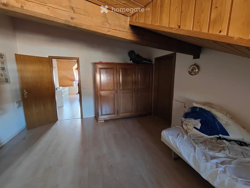 Bedroom with wooden floor, bed with white and blue bedding, wardrobe, and open door leading to another room.