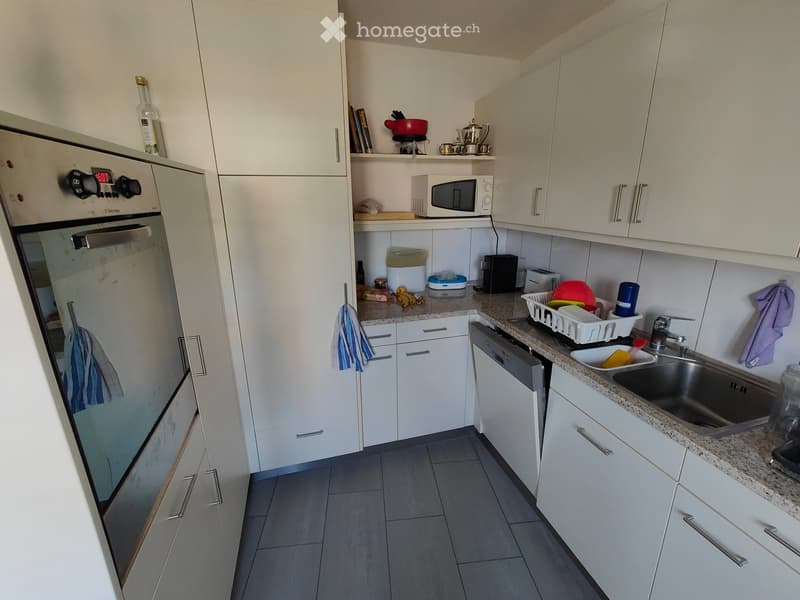 Modern kitchen with white cabinets, granite countertops, stainless steel appliances, and various kitchen items on the counters.