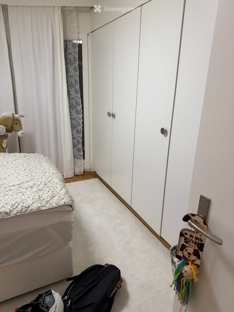 Single bed, white duvet, white rug, white wardrobes, white curtains, toy horse, toys on the door handle.