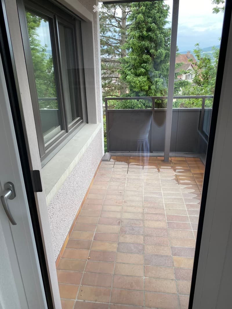 Balcony with tiled floor, metal railing, and a view of greenery and neighboring houses.