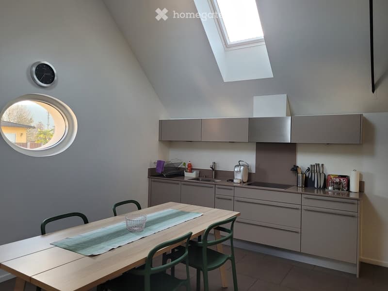 Modern kitchen with grey cabinets, a wooden dining table with green chairs, a sink, and various appliances.