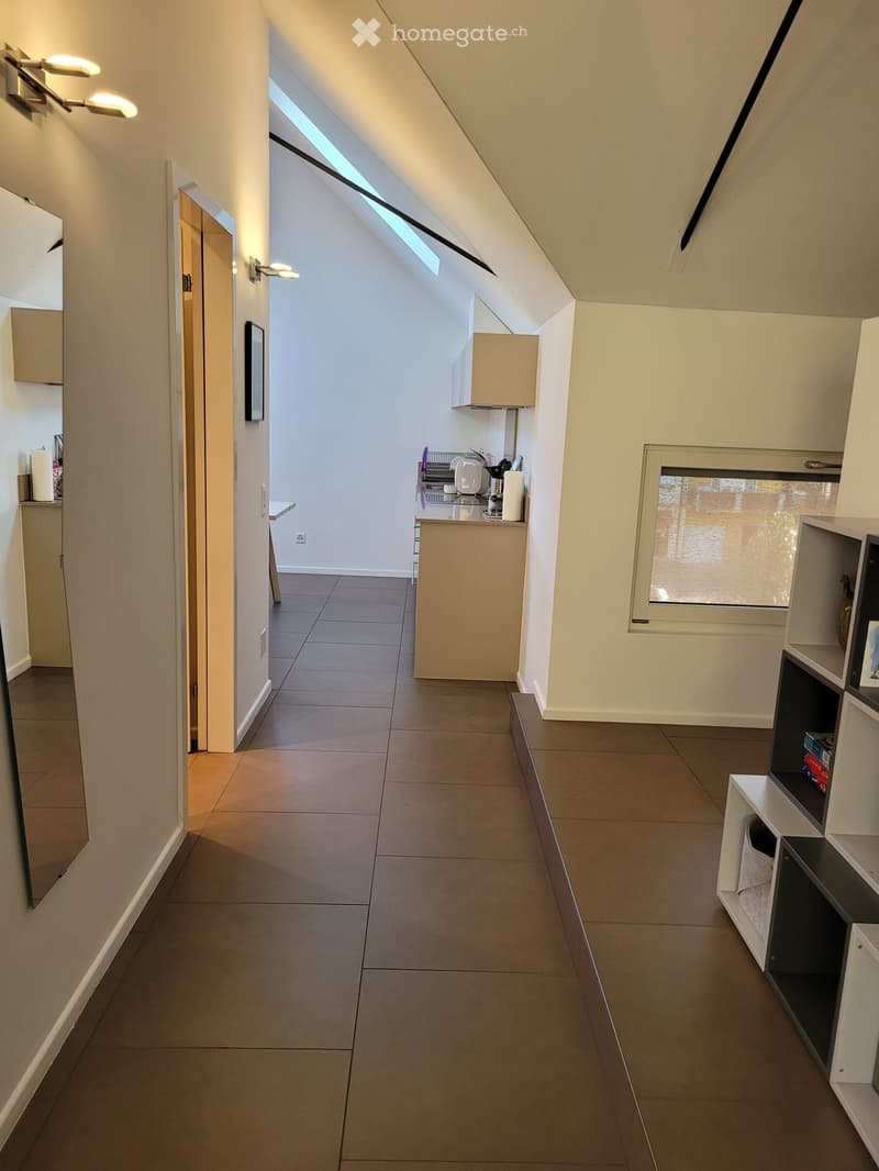 Bright hallway with tiled floor, white walls, built-in shelving unit, and a small kitchenette area visible at the end.