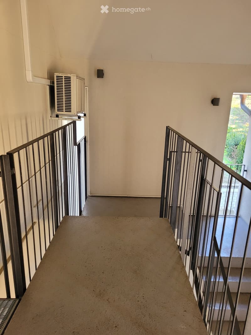 Staircase with metal railings, beige walls, and a concrete landing. An air conditioning unit is mounted on the wall to the left.
