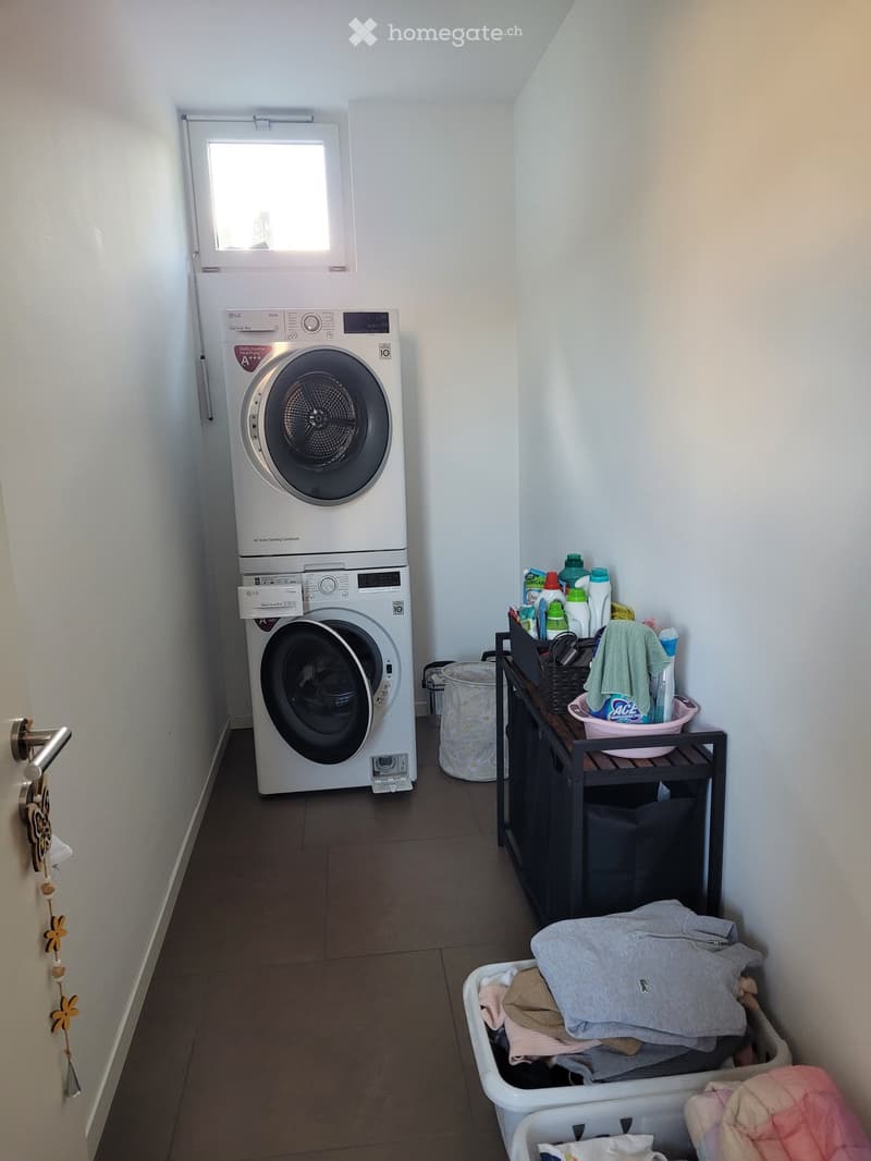 Laundry room with a washing machine, dryer, laundry basket, and a small table holding cleaning supplies and a towel.