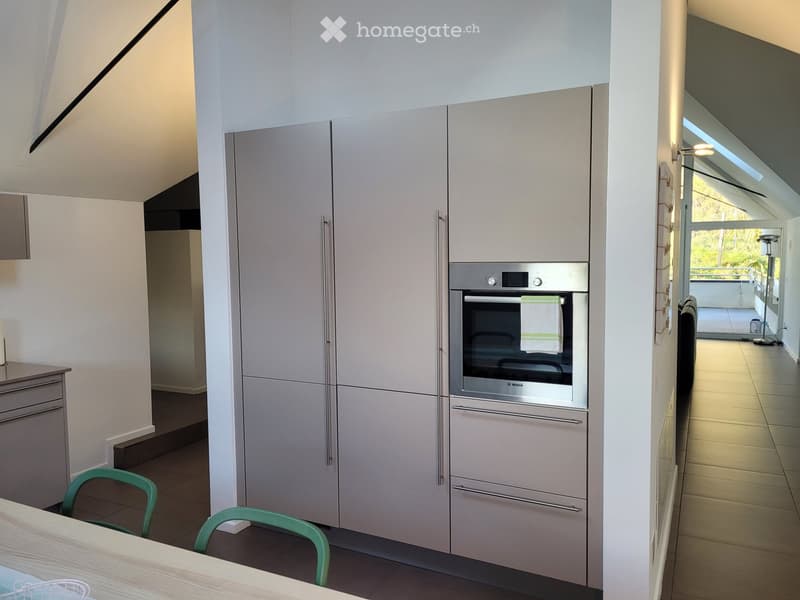 Modern kitchen with light grey cabinets, stainless steel oven, and a small dining area with a table and chairs.
