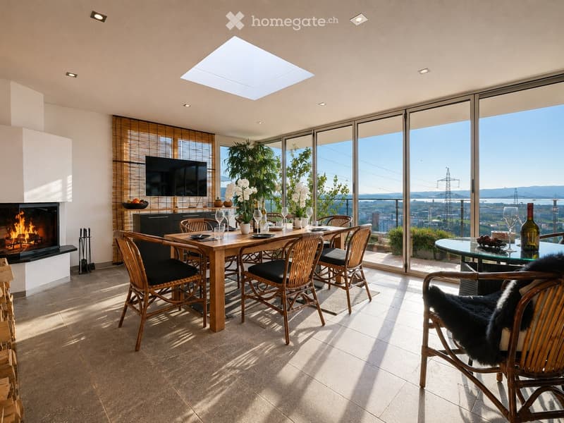 Modern living room with a fireplace, large windows offering a scenic view, a dining table with chairs, and a glass table with wine glasses and a bottle.