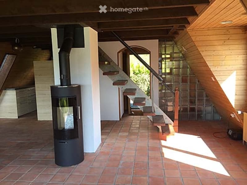 The image shows a wooden staircase leading up to a landing area with a wooden railing and wooden wall. The floor is made of terracotta tiles, and there is a wooden cabinet on the left side. A wooden door and a wooden window are visible in the background,