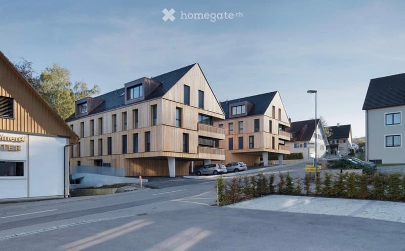 Modern multi-story residential building with wooden facade, balconies, and a covered parking area.