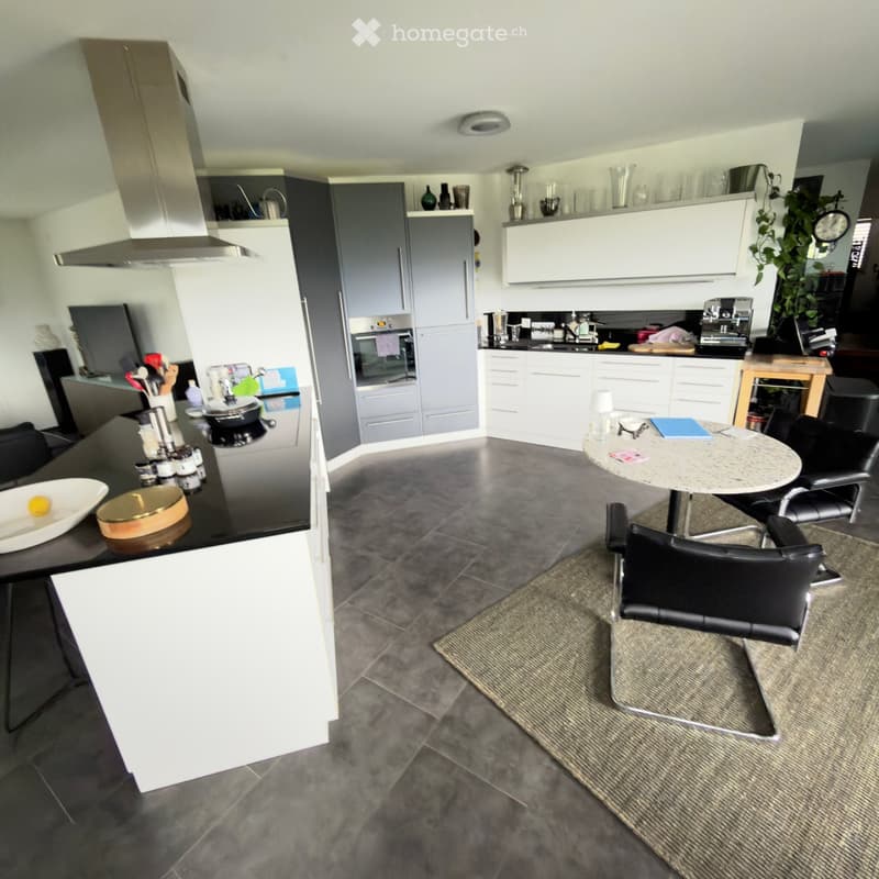Modern kitchen with grey and white cabinets, stainless steel appliances, a central island with a black countertop, and a small dining area with a round table and chairs.